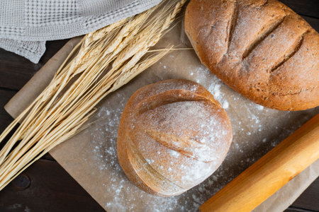 Two artisan bread loaves rest on parchment with wheat stalks and rolling pin, creating a cozy...