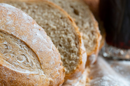 Golden rustic bread loaf partially sliced on wooden surface, paired with a glass of kvass and wheat...