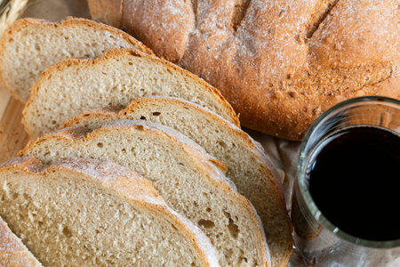 Golden rustic bread loaf partially sliced on wooden surface, paired with a glass of kvass and wheat...