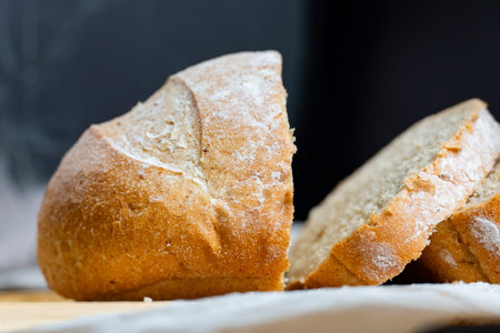 Freshly baked rustic bread loaf partially sliced on wooden surface