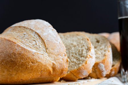Golden rustic bread loaf partially sliced on wooden surface, paired with a glass of kvass and wheat...