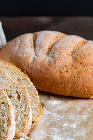 Freshly baked rustic bread loaf partially sliced on wooden surface