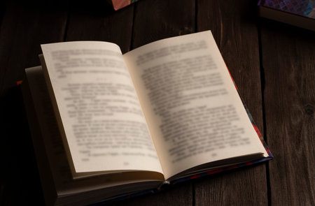 Hardcover book opened on dark wooden surface with blurred pages, creating a cozy rustic atmosphere of reading, study, and creative inspiration