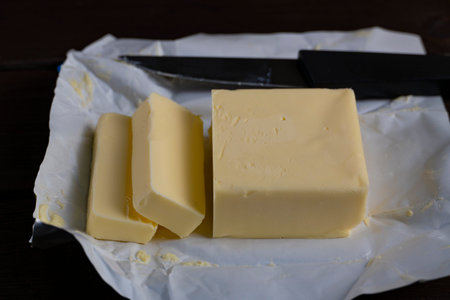 Close-up of fresh butter block with sliced pieces and knife on wrapping paper. Ideal for cooking, baking, dairy, or food blog themes