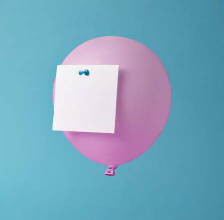 White paper note pinned on pink balloon. Pastel blue background. Minimal concept.の写真素材