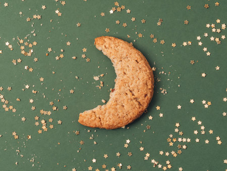 Bite of moon shape cookie biscuit with gold glitter stars on green background. Crescent creative concept.の写真素材