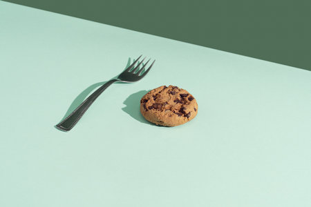 Creative composition with chocolate chip cookie and fork on bright mint background. Hard shadows, minimal vintage table concept with copy space.の写真素材