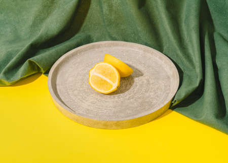 Sliced lemon on grey concrete plate against bright yellow background. Vintage retro scene with green plush curtain.の写真素材
