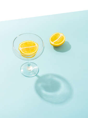 Minimal summer scene with halved lemon in crystal champagne glass on bright blue table.の写真素材