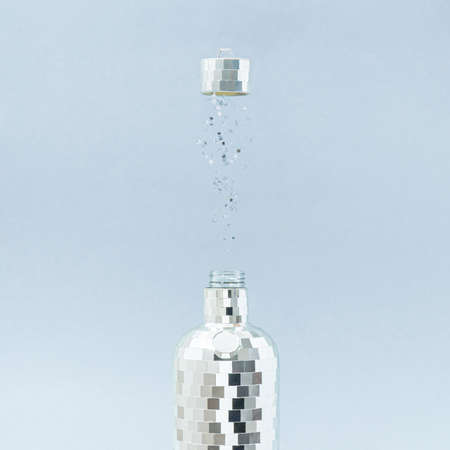 Creative composition with silver alcohol bottle and shiny glitter against grey background. Minimal 2021 party time concept.の写真素材