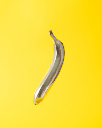 Minimal composition with metallic gray banana against bright yellow. Contemporary cyberpunk fruit background.の写真素材