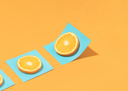 Trendy summer composition with citrus fruit slice on bright blue paper sheet over sunny orange...