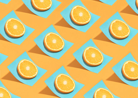 Trendy summer pattern with citrus fruit slice on bright blue paper sheet over sunny orange table....
