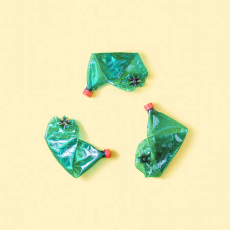 Minimal flat lay with three folded green plastic bottles on pastel yellow background. Creative ecology conceptの写真素材