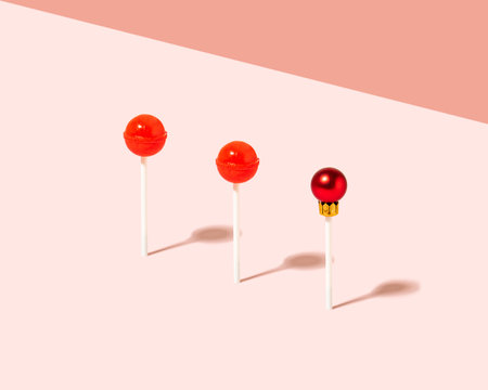 Creative composition with tasty red lollipops and Christmas bauble against pastel pink background.  Minimal xmas candy concept.の写真素材