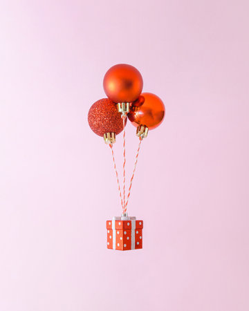 Creative composition with levitating three red Christmas decorations and giftbox. Trendy holiday shopping concept.の写真素材