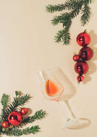 Creative Christmas party flat lay with rose vine glass, fir branches and red baubles on bright cream background with copy space. trendy xmas template.の写真素材