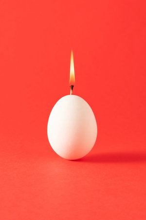 Minimal easter composition with lighted egg candle against vibrant red background.