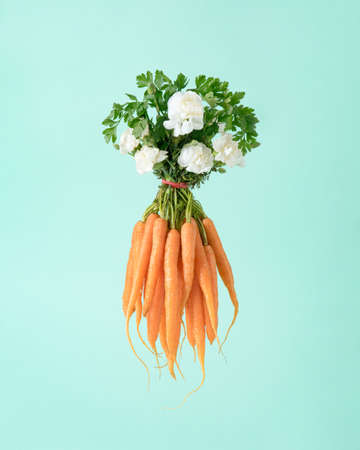Creative composition with bouquet made of flowers and carrots against pastel olive green background. Minimal organic food concept.の写真素材