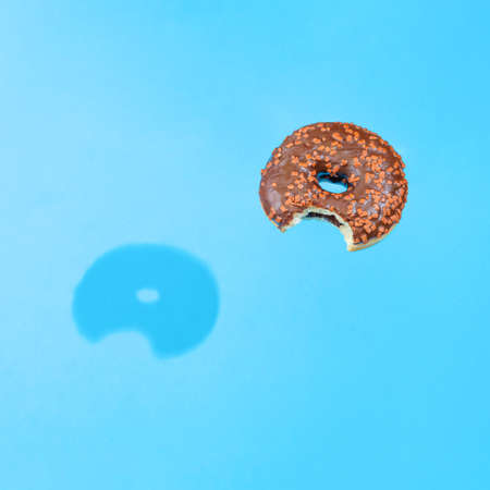 Trendy composition with bitten chocolate donut and bright blue background.の写真素材