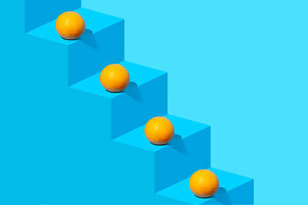 Creative composition with fresh orange fruit on blue staircase. Creative copy space. Next level concept.の写真素材