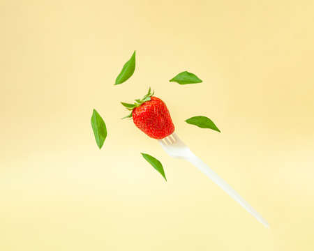 Creative composition with levitating green leaves and red strawberry on a white fork. Healthy food concept.の写真素材