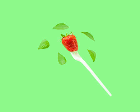 Creative composition with levitating green leaves and red strawberry on a white fork. Healthy vegan food concept.の写真素材
