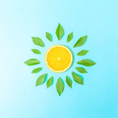 Minimal composition with fresh orange slice and green leaves on pastel blue background. Creative summer scene. Vegan concept.の写真素材