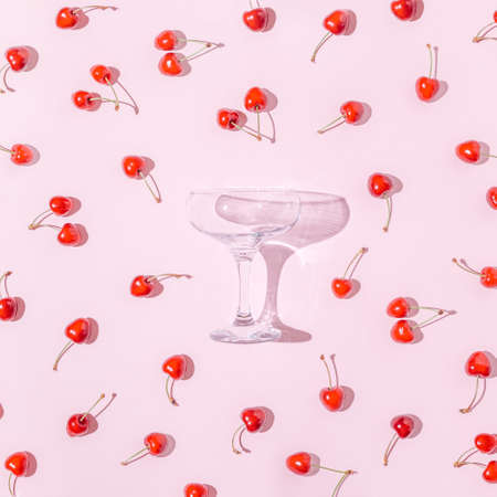 Trendy flatlay with knocked down cocktail glass and lots of fresh cherries on bright pink background.の写真素材