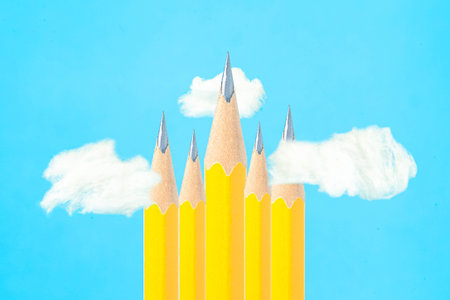 Creative composition with sharp yellow wooden pencils and white clouds against blue background. High...
