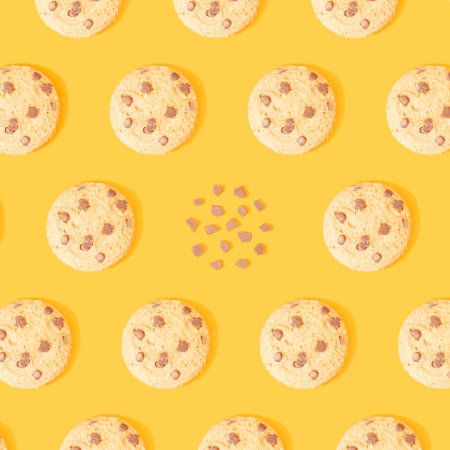 Creative pattern with tasty chocolate chip cookies and crumbs on mustard yellow background. Be...