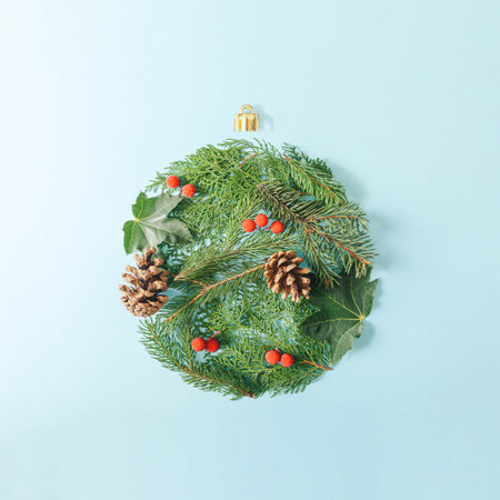 Minimal christmas flat lay composition with green fir branches, cones and red berries on serenity pastel blue background. Christmas bauble shape.の写真素材