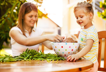 Mother and daughter enjoying outhside and peeling peas off.の写真素材