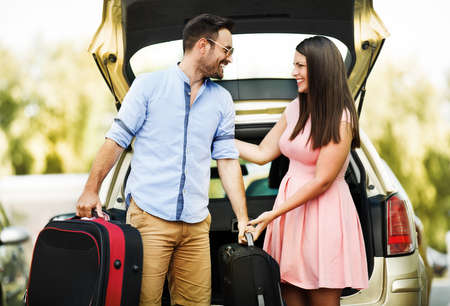 Happy couple putting suitcases into a trunk.の写真素材