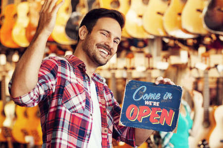 Musical intruments store. Young sale person is showing open store sign.の写真素材