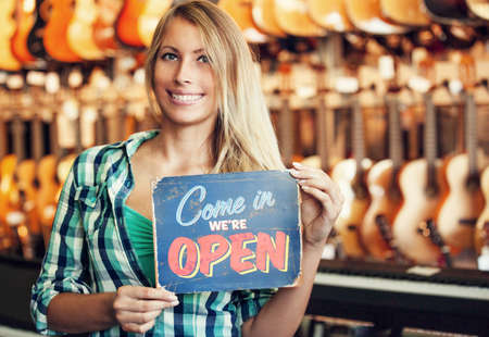 Musical intruments store. Young sale person  is showing open store sign.の写真素材
