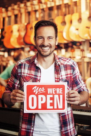 Musical intruments store. Young sale person is showing open store sign.