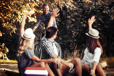 Group of friends is sitting on stump while their friend is coming with bike.の写真素材