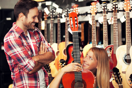 Young woman is looking for guitar in musical instruments store.の写真素材