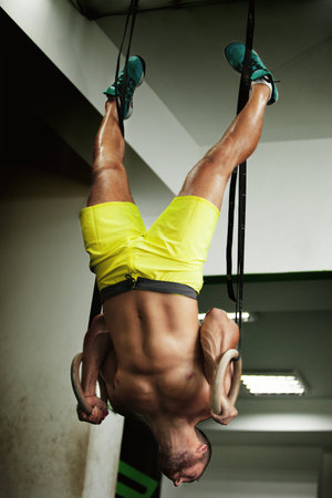 Young fit man pulling up on gymnastic rings.