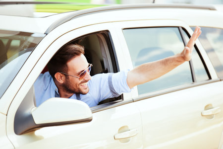 Young man driving a car and greeting to someone.