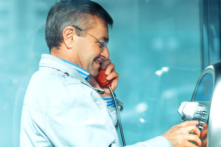 Handsome senior man talking on the phone in a phone booth