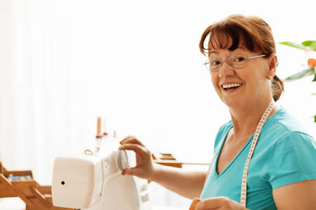 Senior woman sewing at home early in the morning.の写真素材