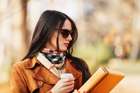 Beautiful young woman is having coffee break in the park. 