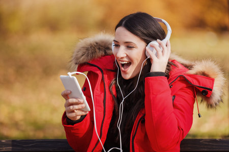 Beautiful young woman using cellphone and headset in the park. 