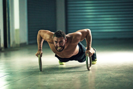 Young stron man is doing push-ups by rings.