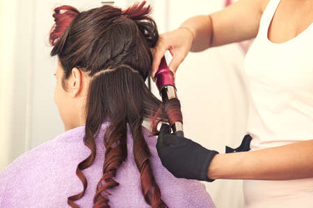 Young woman at hairdresser. Hairdresser is curling her hair.の写真素材