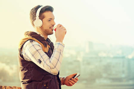 Young handsome man is enjoying outdoor and drinking coffee.の写真素材