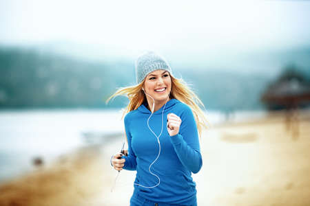 Young blonde woman is jogging and listening music on the beach.の写真素材