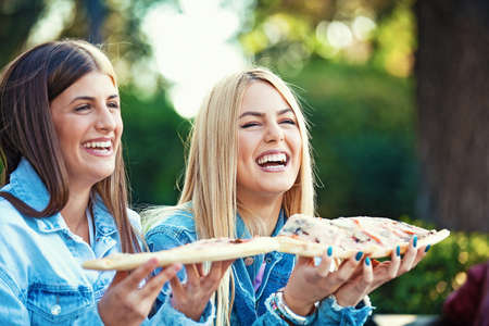 Happy young women having fun in the park and eating pizza.の写真素材